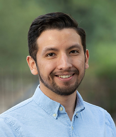 Portrait of Jose Agular - a man with a blue shirt and brown hair smiles at the camera