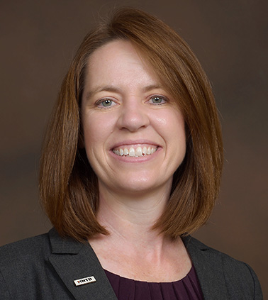 Portrait of LeAnne Napolillo - young brunette woman wearing dark blouse smiling at camera