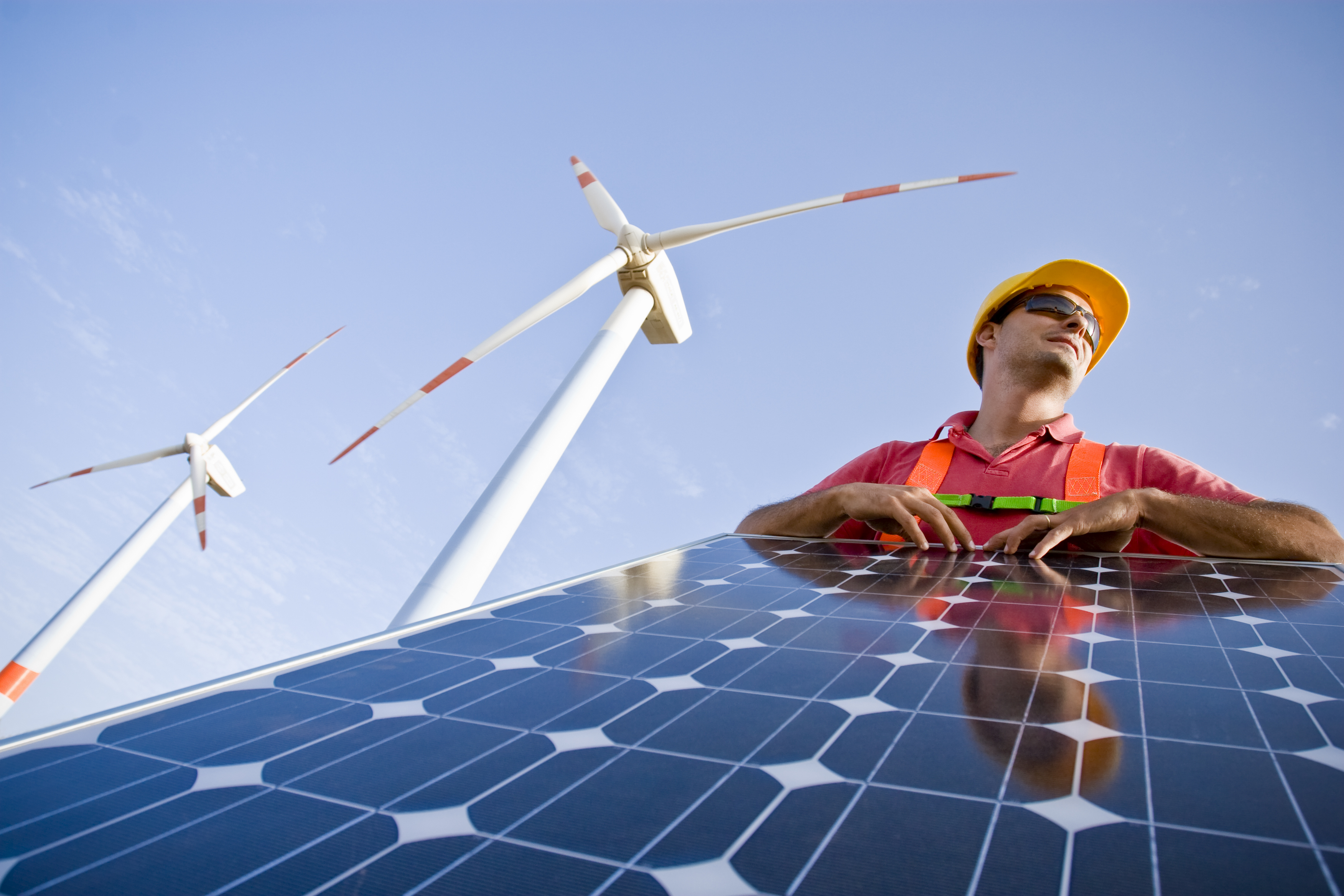 An engineer leaning on a solar panel with two windmills in the background.