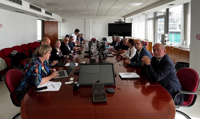 Pictured: Fifteen people sitting at a conference table having  a meeting