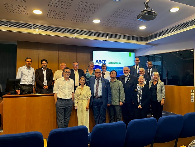 Pictured: Sixteen people standing in front of a screen, smiling at the camera. 