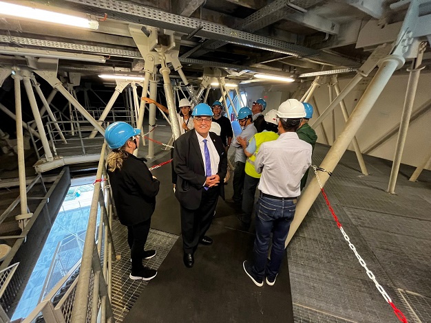 Pictured: Nine people with hard hats on at a construction site. One person is facing the camera and smiling. 