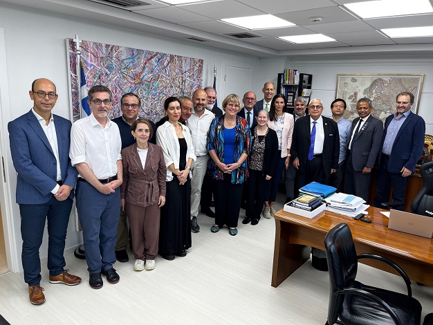 Pictured: Eighteen people standing in a room smiling at the camera. 