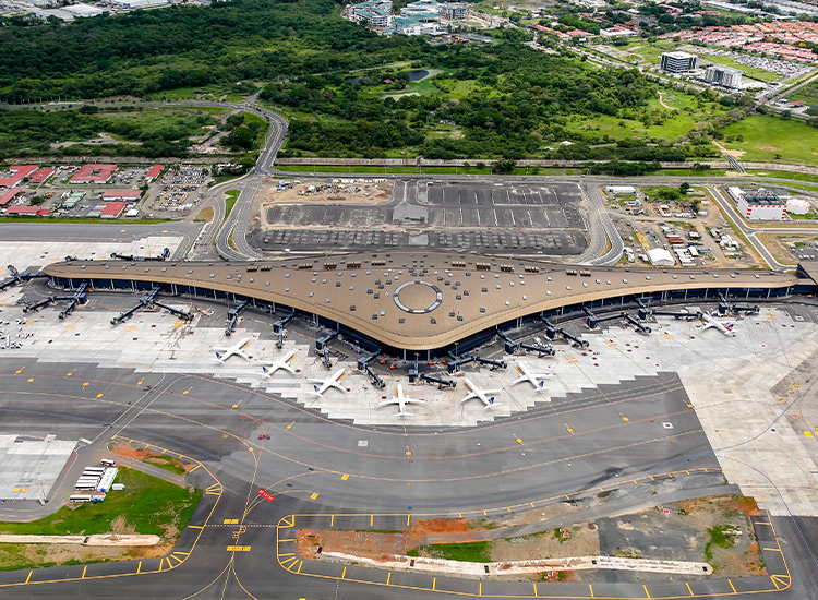 Image shows an airport terminal that is shaped like an aircraft ring. There are many planes parked around the terminal. 