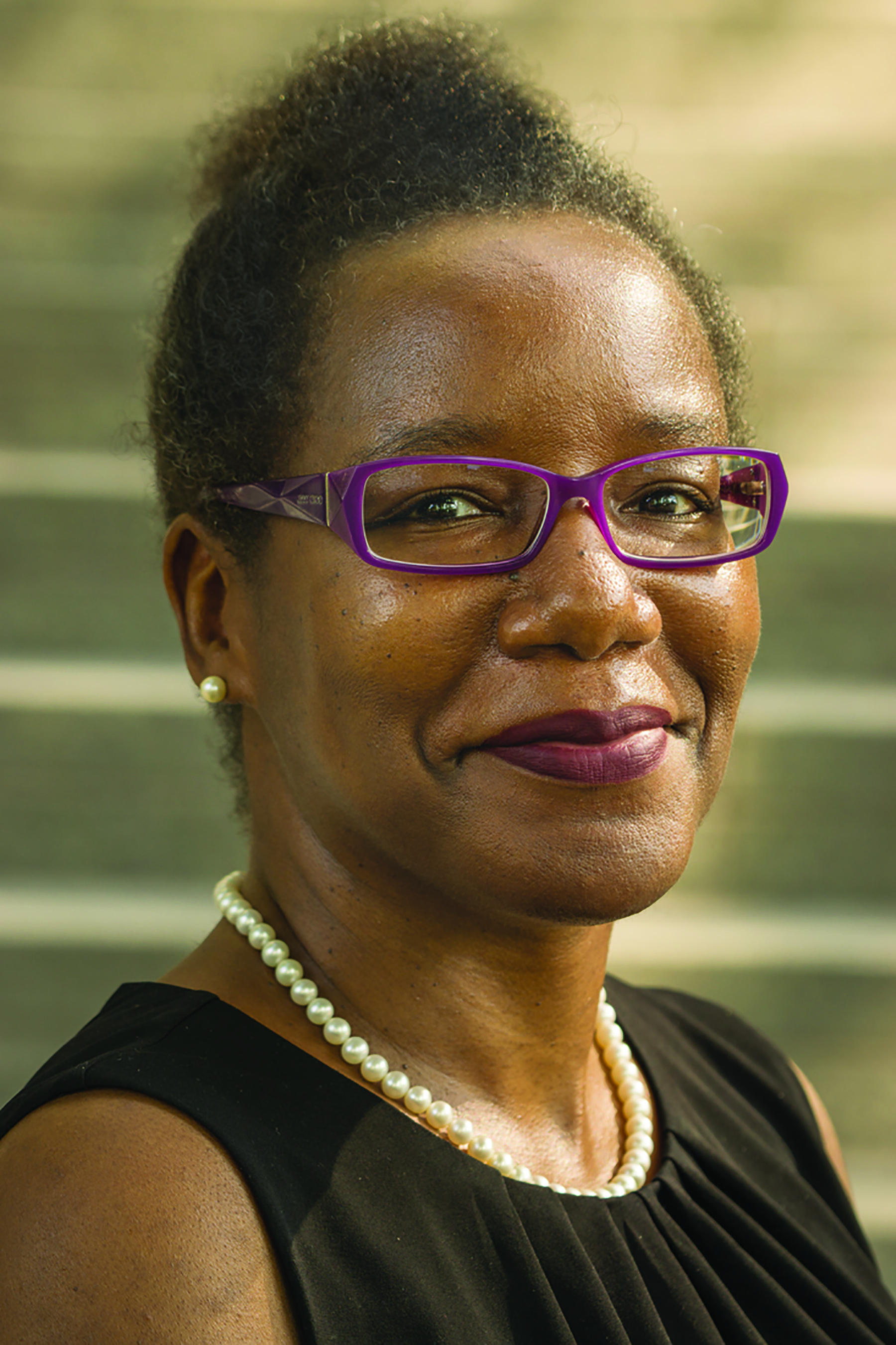 Woman with brown skin wearing a black, sleeveless blouse smiles at the camera.