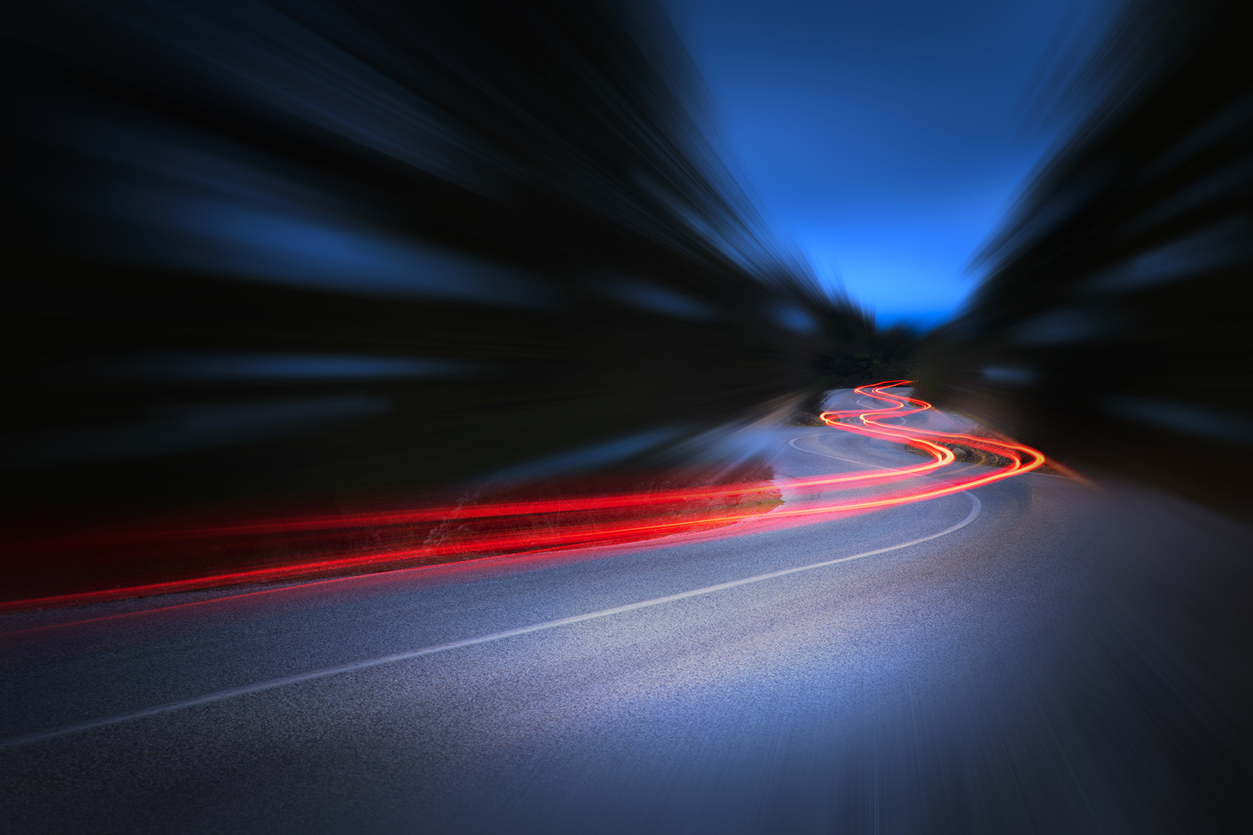 Cars leave curvy red trails on a road at night.