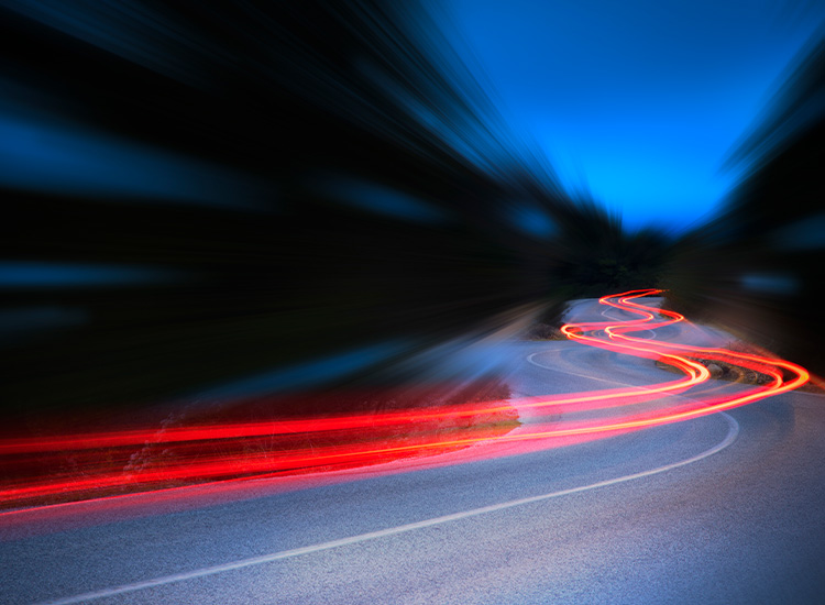 Cars leave curvy red trails on a road at night. 