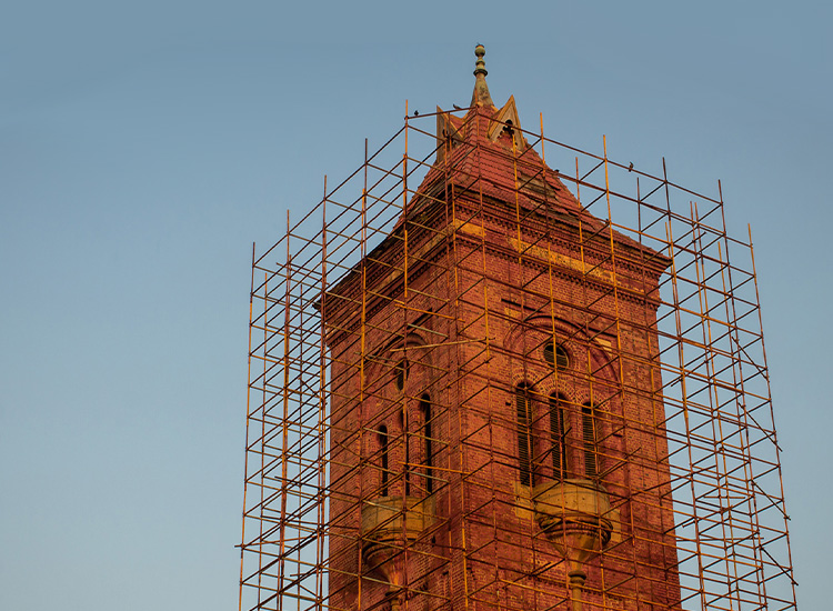 Tall, red brick tower is surrounded by scaffolding. 