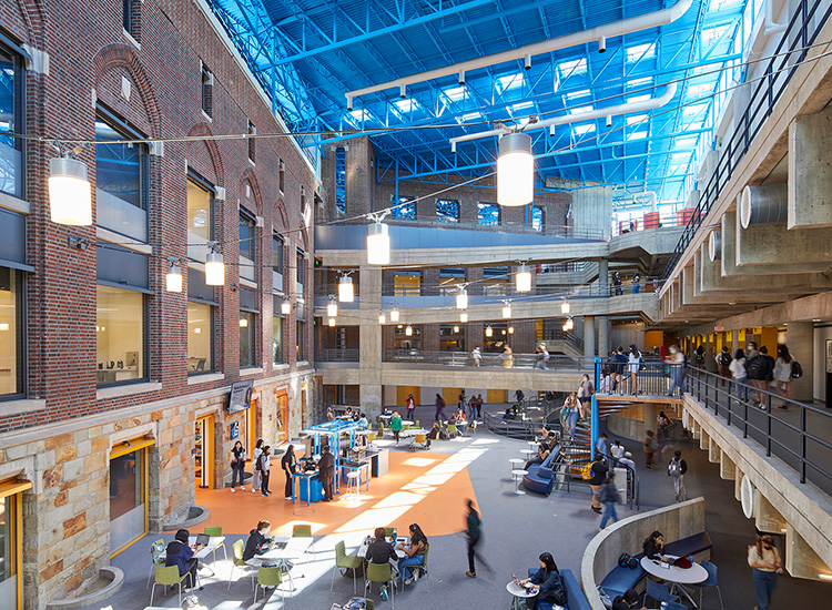 A large, open, multistory space with enclosed walls and elevated walkways. There are many women walking around, seated, and standing within the space. 