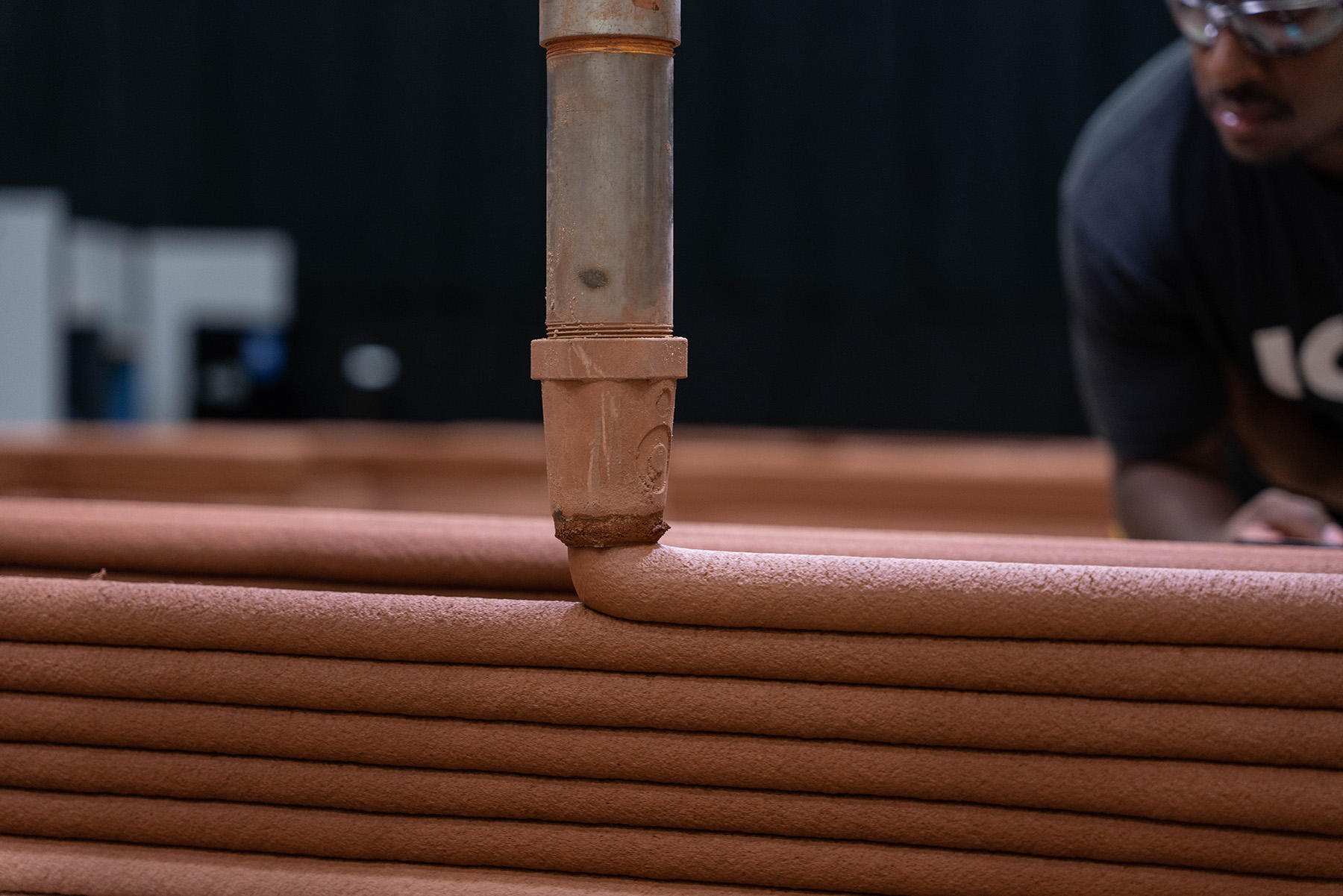 The nozzle of a 3D printer ejects a red substance in layers.