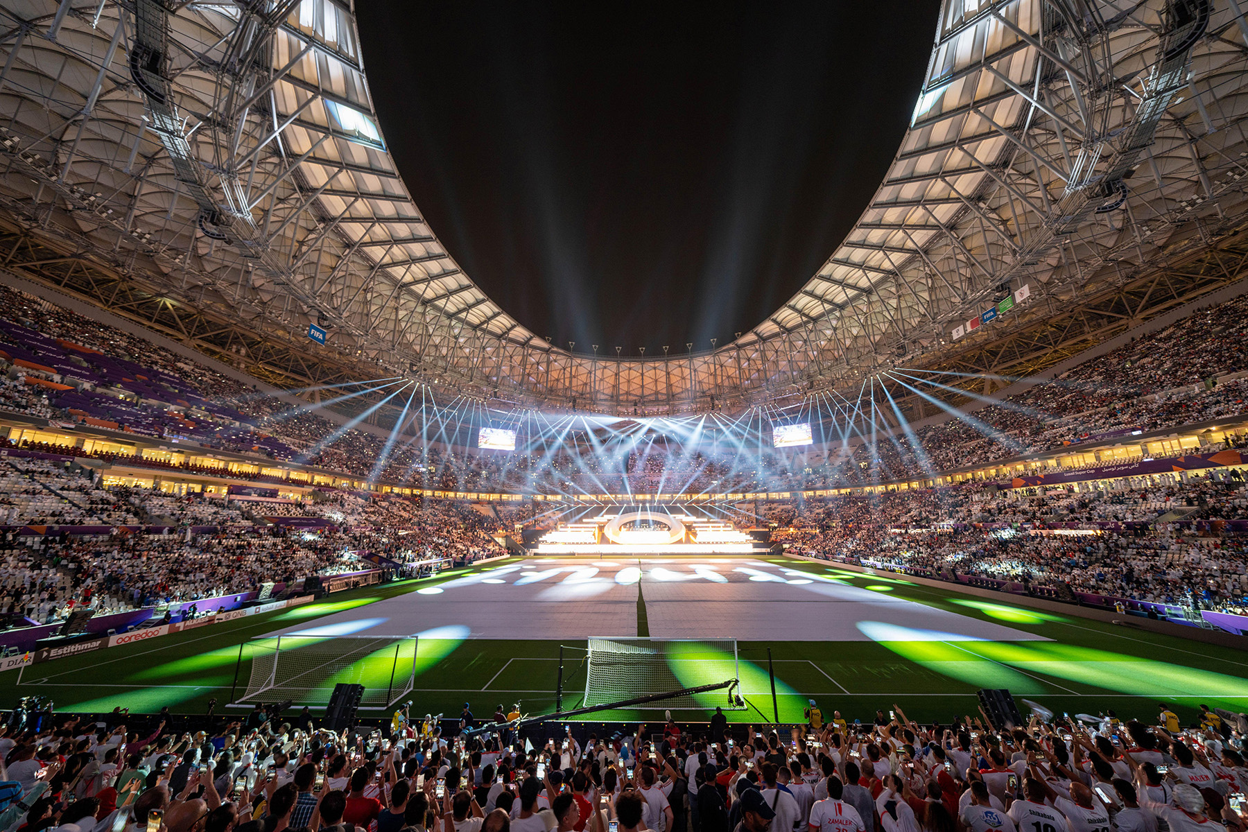 The photograph shows a soccer stadium filled with people and spotlights.