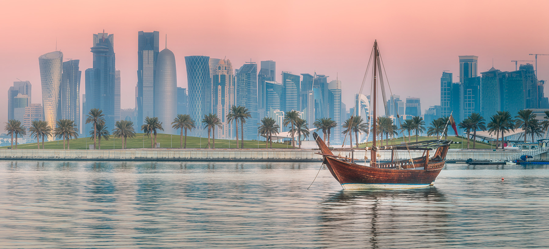 The photograph shows a dhow, an Arabian boat that inspired the design of the Al Janoub stadium, sailing on water with an urban skyline in the background.