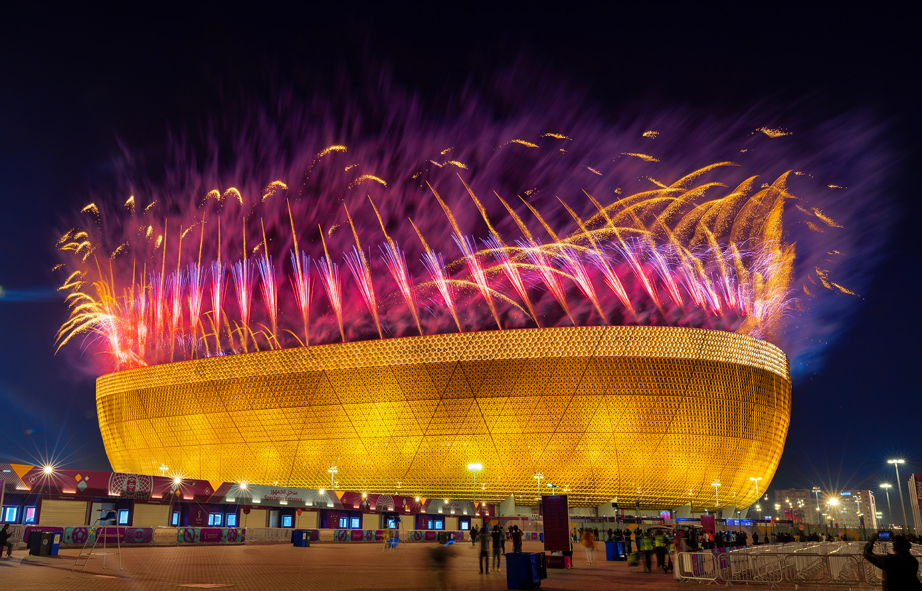 The photograph shows fireworks exploding in the air above the Lusail Stadium at night.