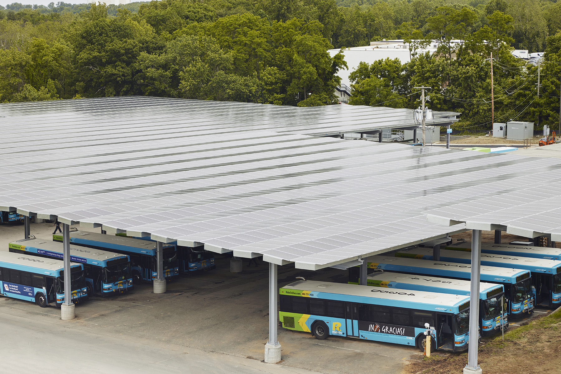 The photograph shows electric buses beneath a canopy covered in solar panels.