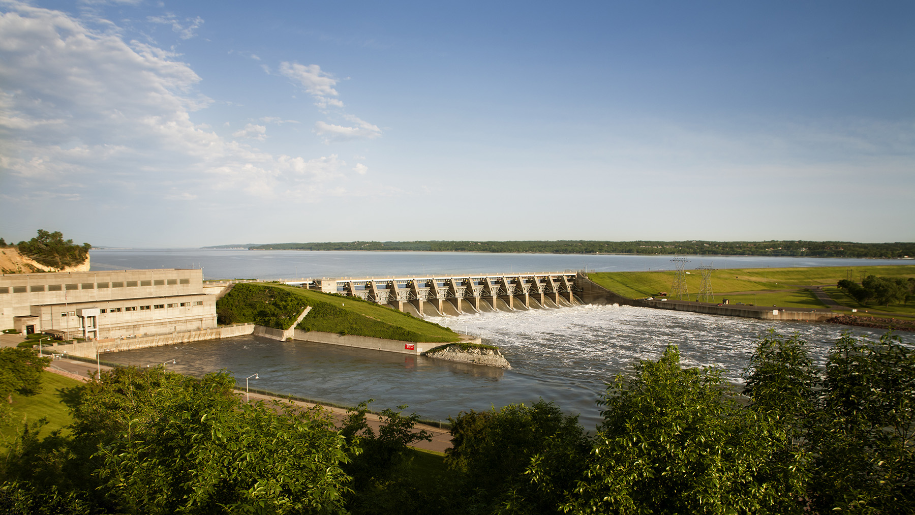 ): Image shows a lake impounded by a dam. Water rushes through the dam’s gates.