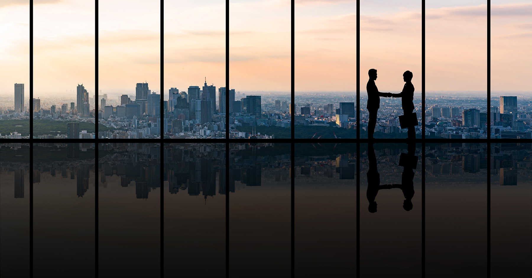 A city skyline is highlighted against the sunset. Two executives are shown shaking hands in silhouette. 