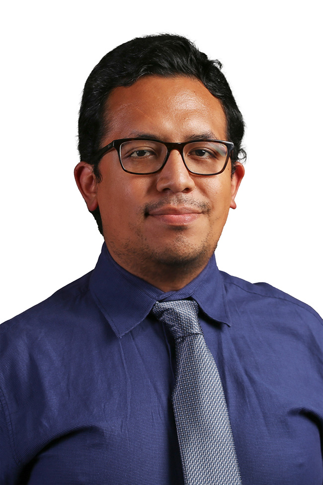 Man in blue shirt and tie smiles at the camera. 